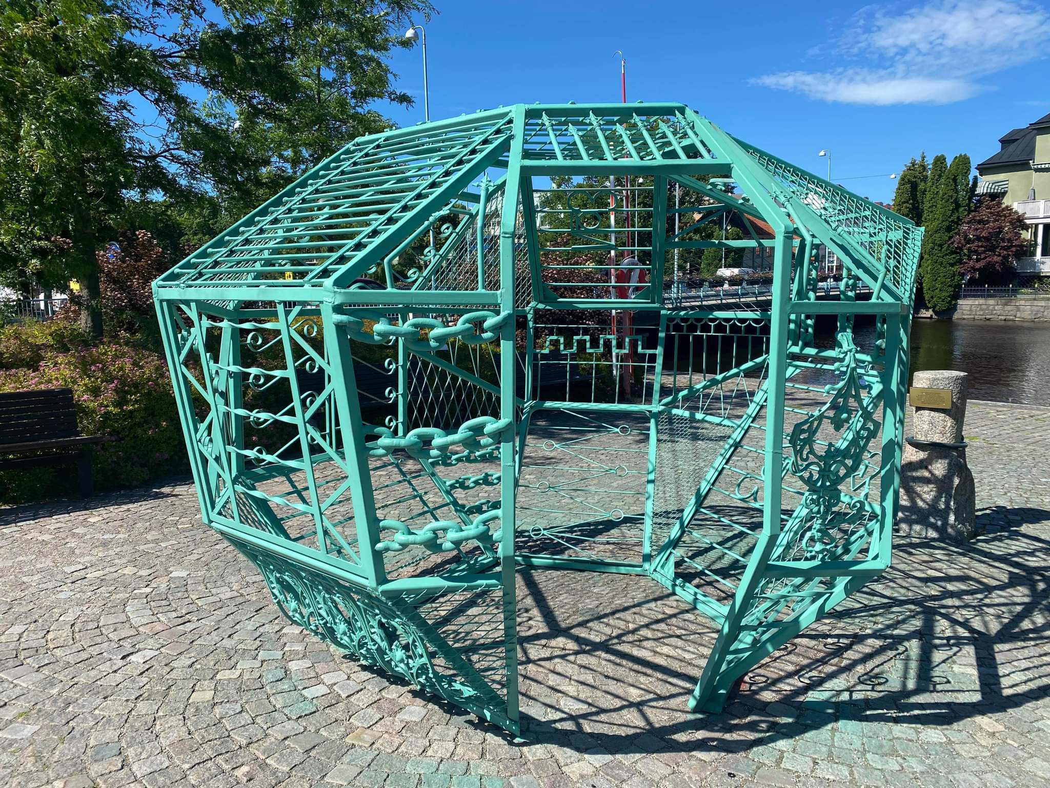 A turquoise steel cage made up of different fences welded together as a globe that you can walk into.