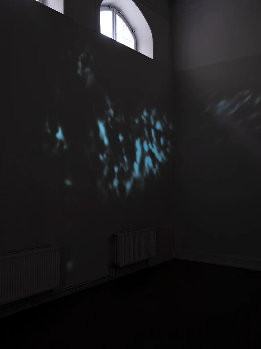 En projektion av ett blåaktigt ljusspe visas på en mörk vägg i ett nedsläckt konsthall.