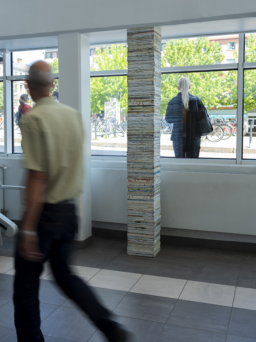 I passagen in till ett köpcentrum är en cirka 2 meter hög pelare placerad. Pelaren är gjord av målardukar/tavlor