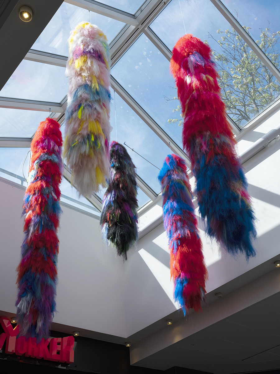 Från ett tak under några stora takfönster i en galleria hänger en installation bestående av flera långa hårtofsar i olika färger. De är olika långa och skiftar i olika starka nyanser, så som rött, blått och svart. De påminner om päls i texturen.