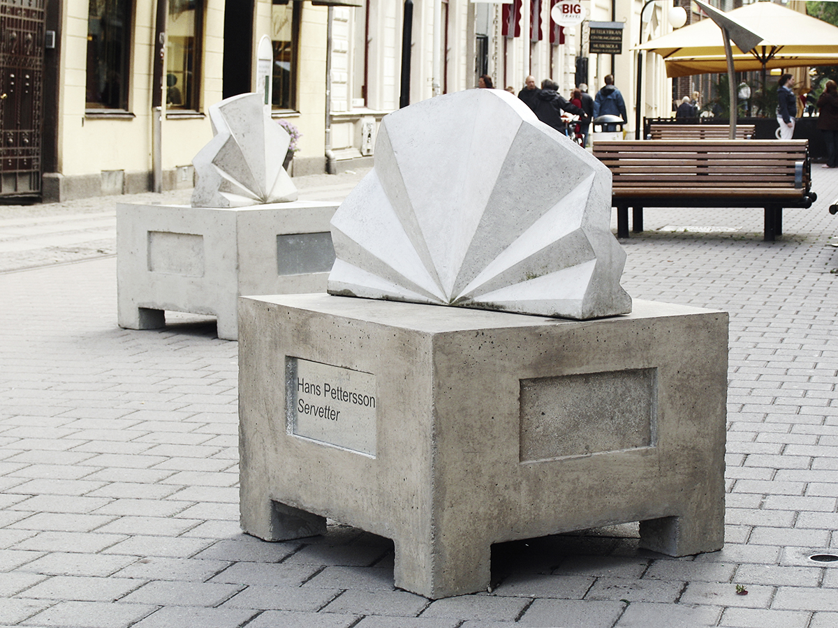 På Kungsgatan står två betongbord och över dem står två betong statyer som föreställer en fint vikt servett som står upp.