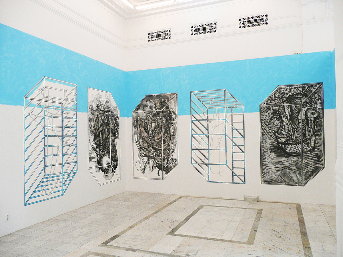 I ett hörn av ett rum är väggarna målade vita nertill och blåa upptill. Målade konstverk sitter på väggarna och föreställer fem boxar samt inuti tre av dem är svartvita målningar.
