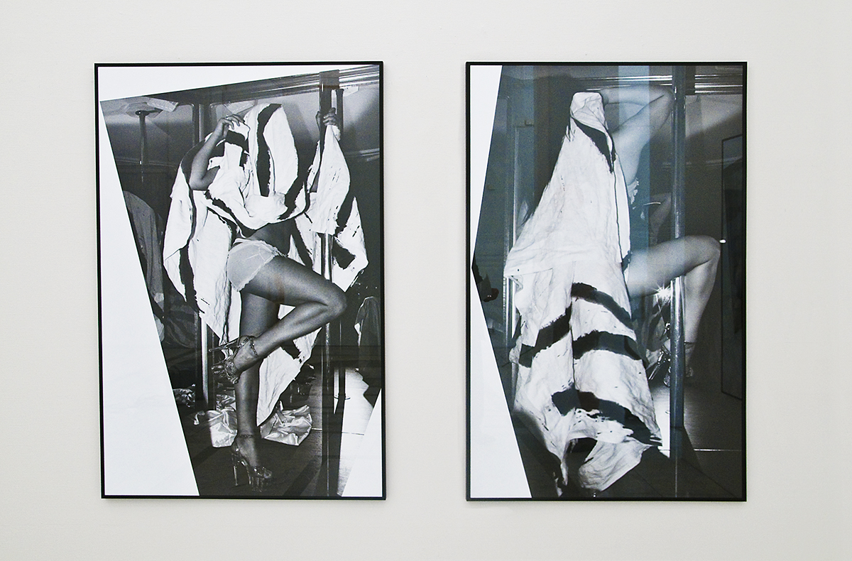 På en beige färgad vägg hänger två svartvita fotografier inramade. Fotona föreställer en kvinna i underkläder och högklackat hon står runt en strippstång och har ett svartvitt lakan över sig.