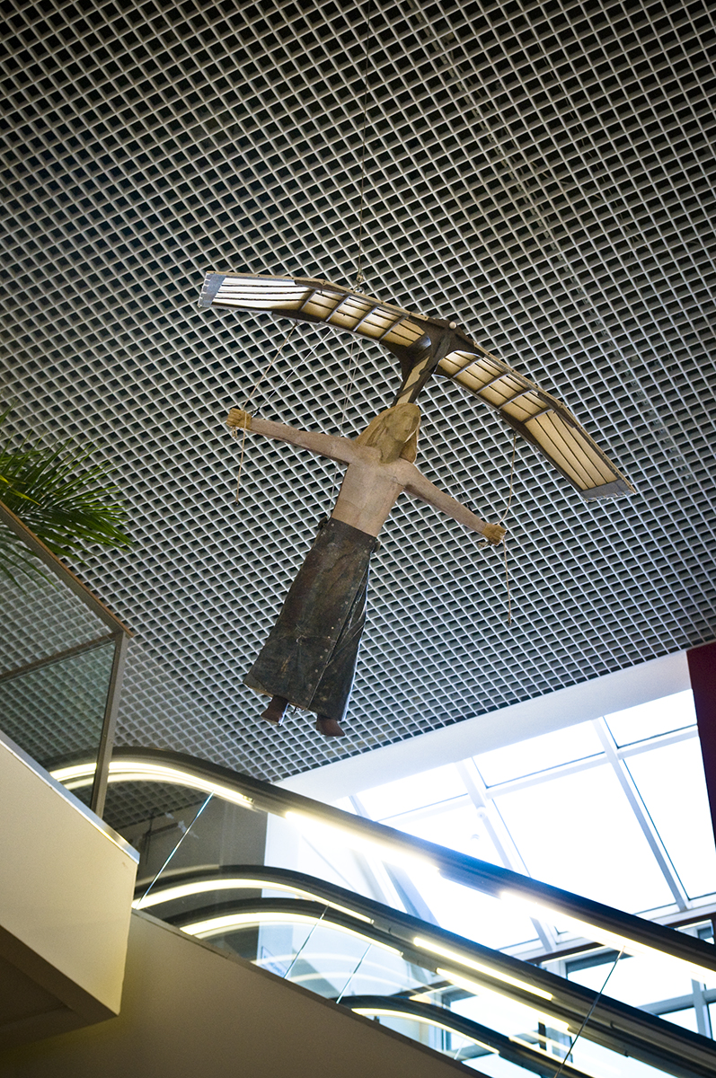 Fotot föreställer en rulltrappa som går upp och uppe i taket hänger en skulptur av en flicka som flyger då hon har en robotliknande fågel på sitt huvud.
