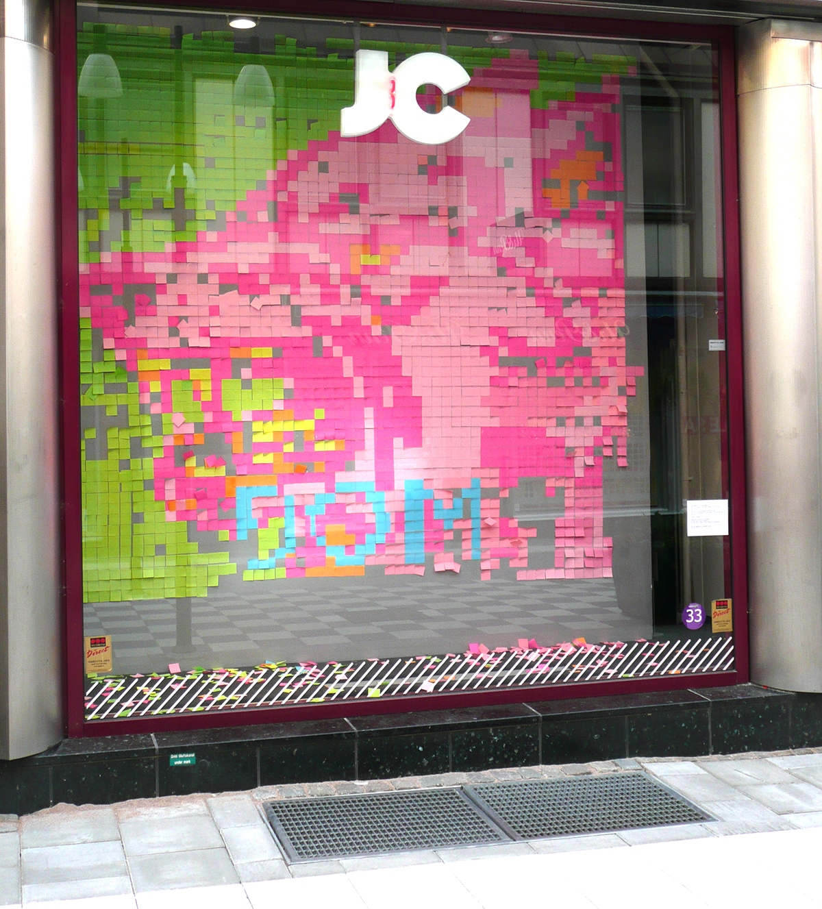 Butiken JCs skyltfönster har blivit utsmyckad med rosa, ljusrosa, gröna, gula samt orangea post-it lappa. Lapparna bildar porträtt som sakta börjar upplösas då limmet släpper och lappen faller till marken.