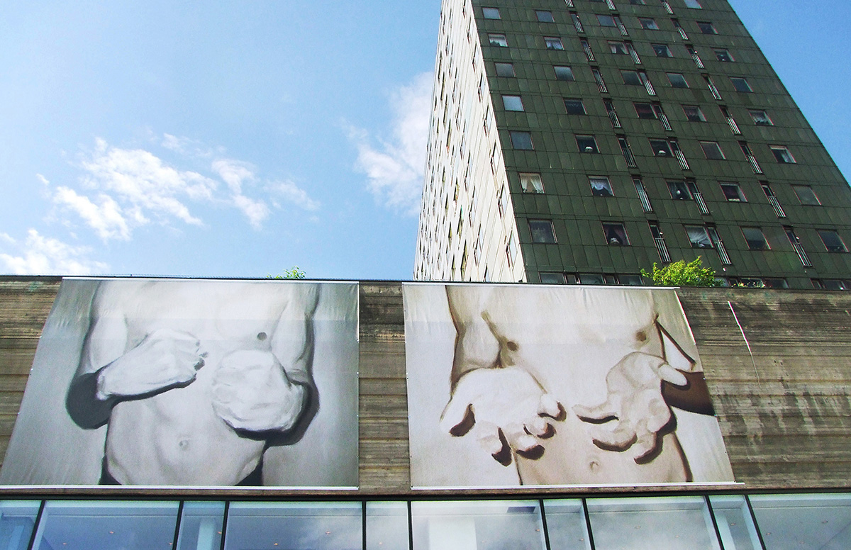 Högst upp på Krämaren fasad hänger två vepor föreställande fotografier på en mans avklädda överkropp med hans händer i fokus.