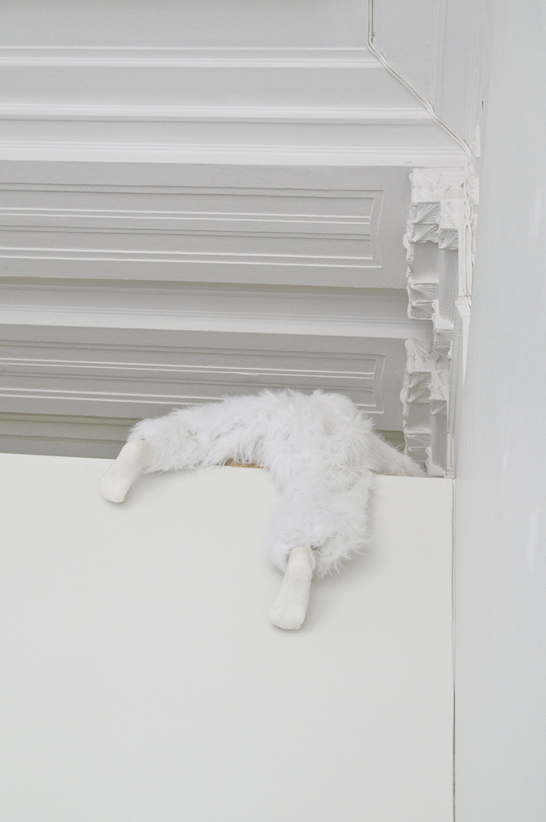 Uppe på en vägg hänger en vit hårig varelse som försöker klättra över väggen.