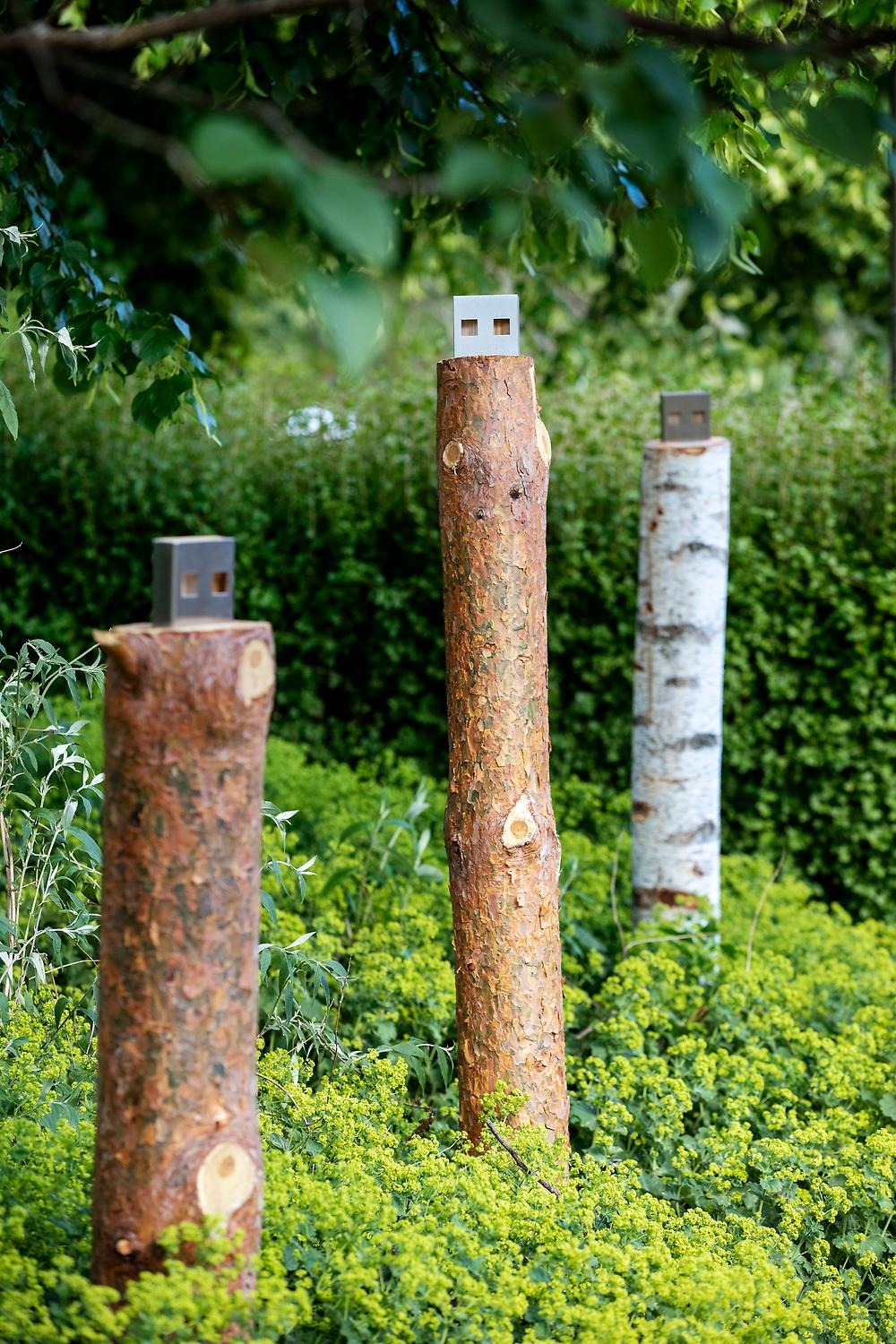 In a park area, three wooden logs stick up, at the top of the logs are metal objects that represent a USB stick that you insert into the computer.