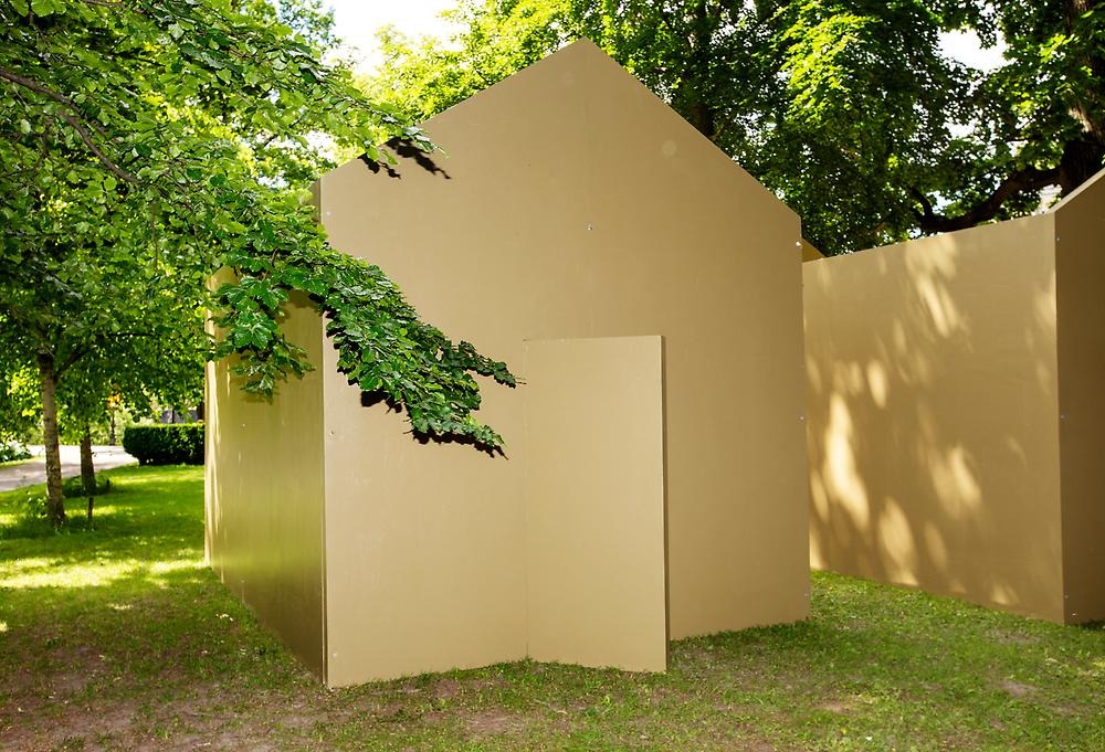 A brown-painted house structure is visible in a park. There is a door on the short side that is half open.