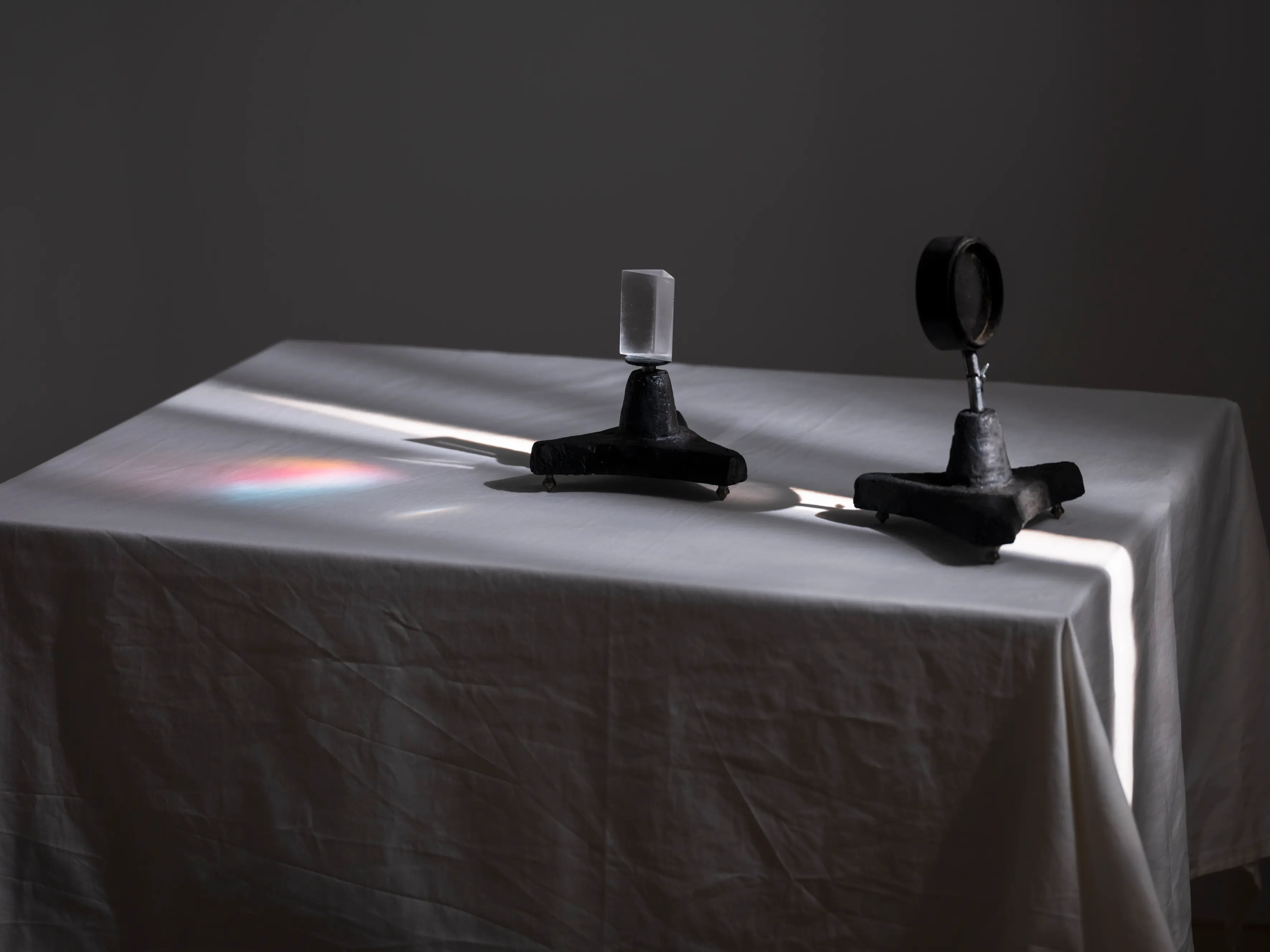 Två objekt står på ett bord med vit duk, solen lyser på objekten från vänster