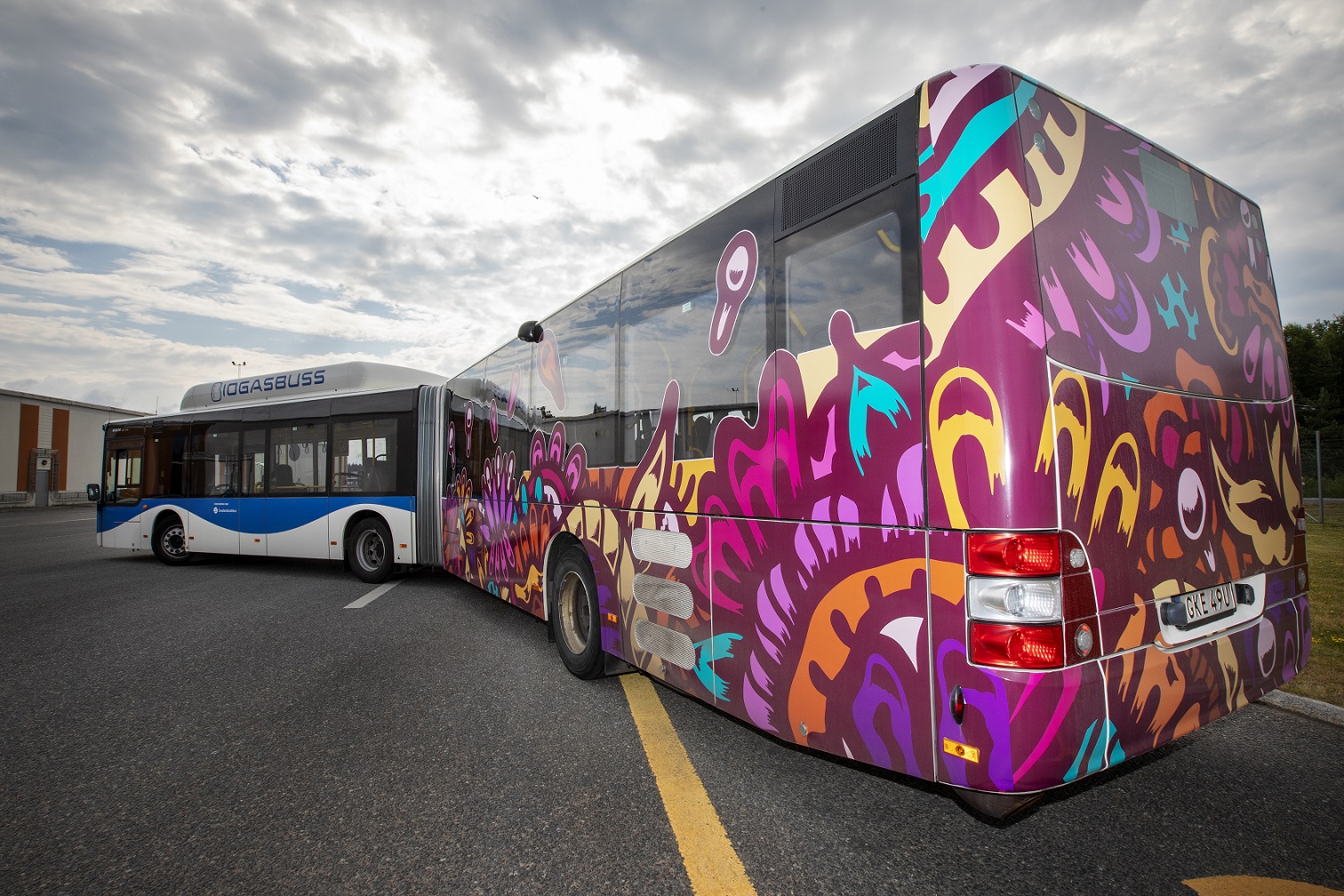 En av stadens stadsbussar, en ledbuss som har ena halvan utsmyckad med ett mönster i olika former och färger främst lila. 