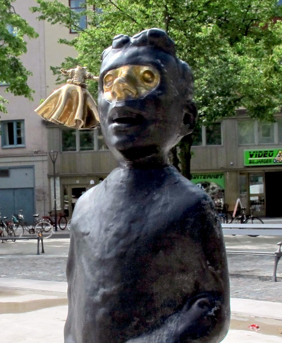 En svartbrun staty av en pojkes byst, hans ögonparti är färgat guld.