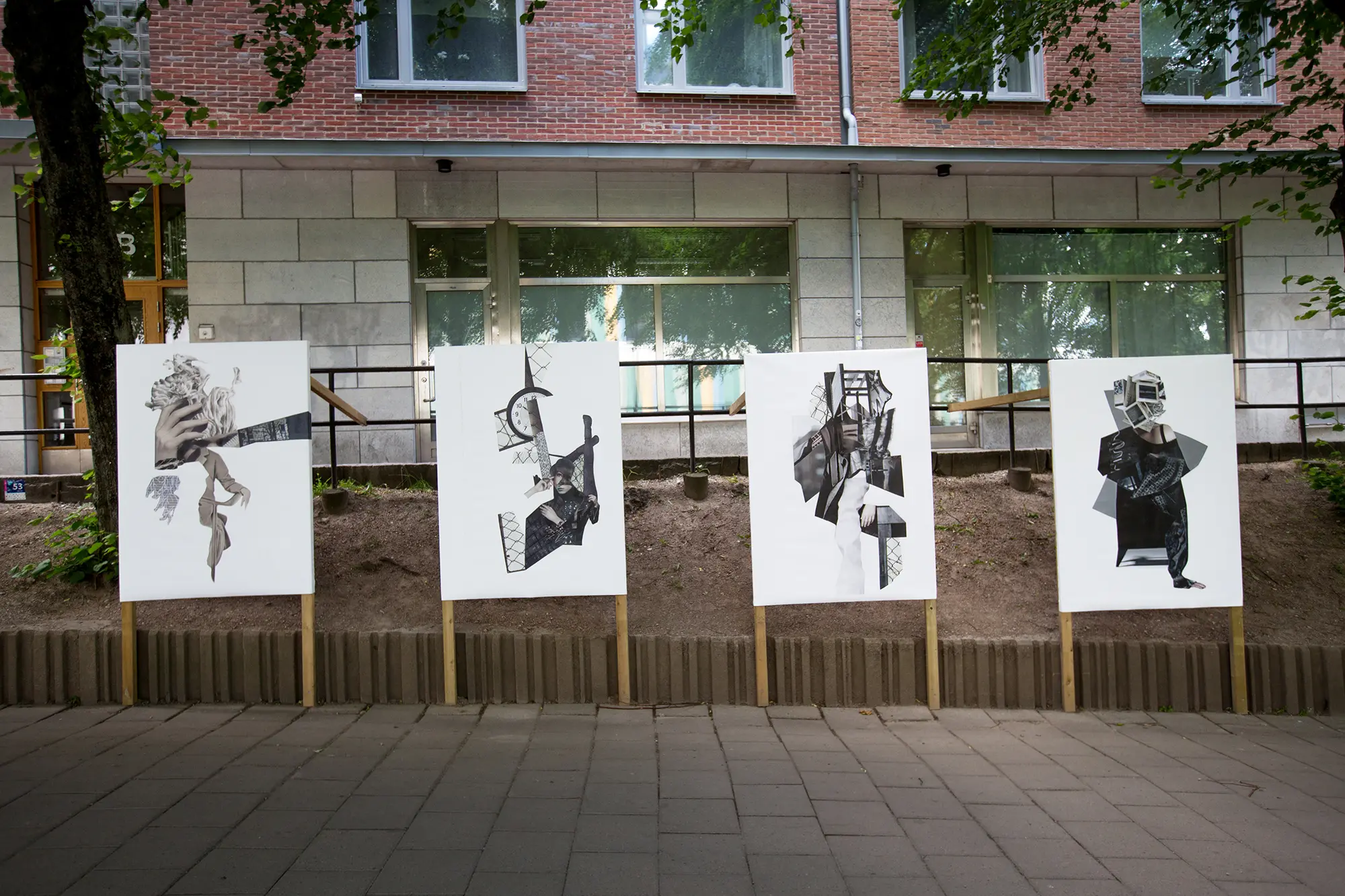 På en gata framför en husfasad står fyra stora svartvita bildkollage uppställda på träpinnar. På kollagen syns olika abstrakta kompositioner av olika utklippta motiv från fotografier, bland annat en hand, en klocka och människor.
