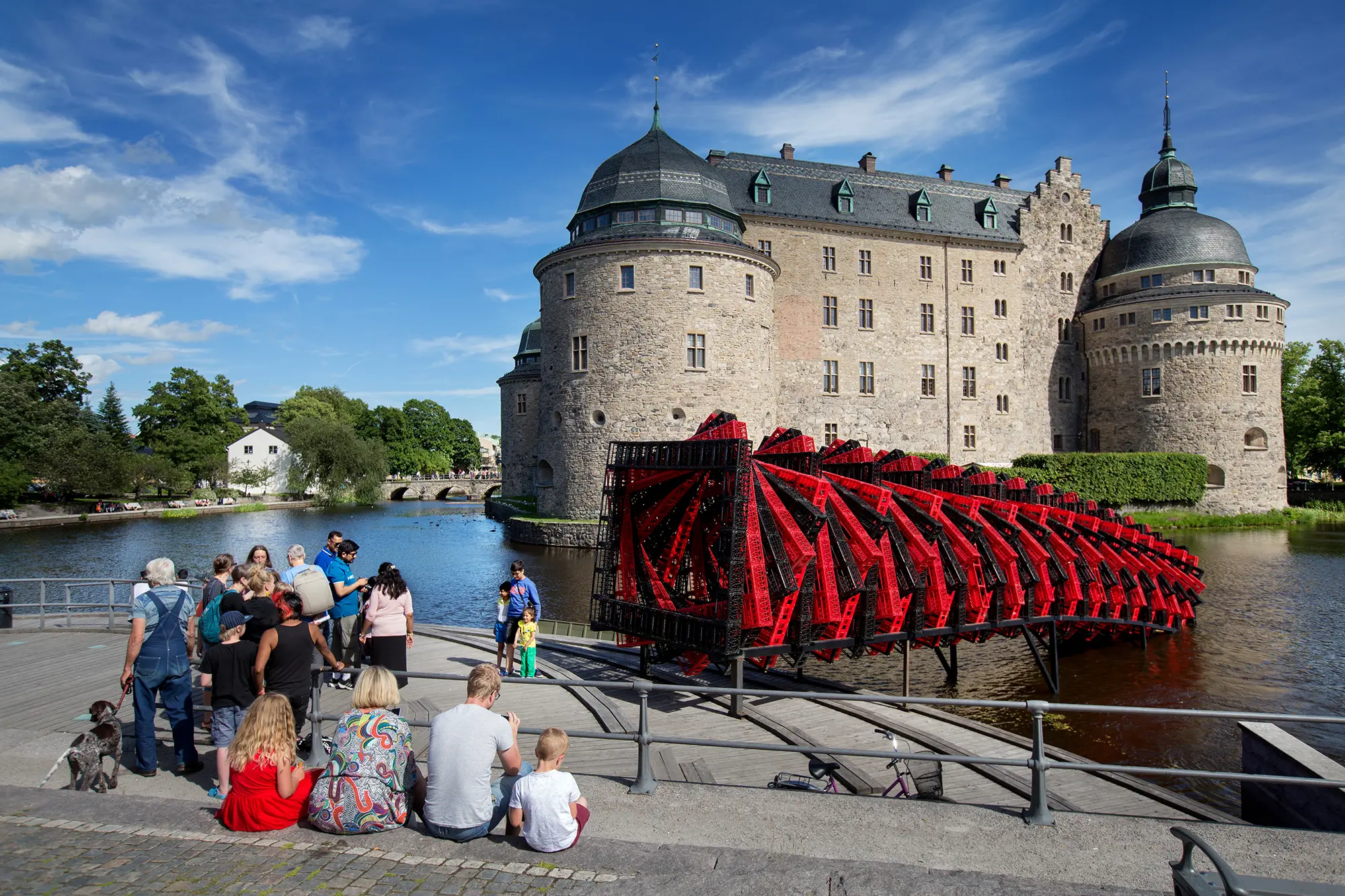 Framför Örebro slott syns en stor skulptur i formen av en tät spiral uppbyggd av röda och svarta plastlådor. Till vänster syns människor som står framför skulpturen och tar kort.