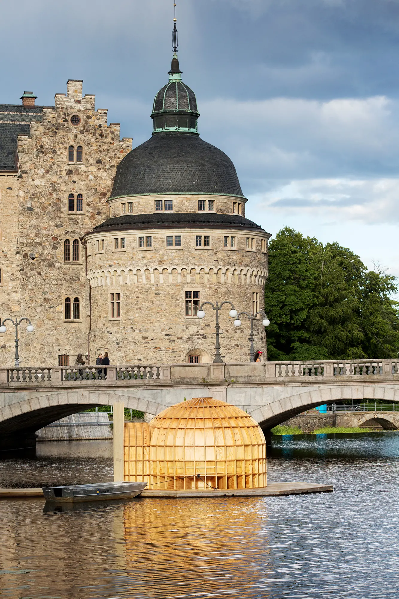 På en plattform i vattnet framför Örebro slott syns en stor träskulptur i plywood som är kupolformad. Skulpturen har en ingång på ena sidan och framför den ligger en roddbåt förtöjd.