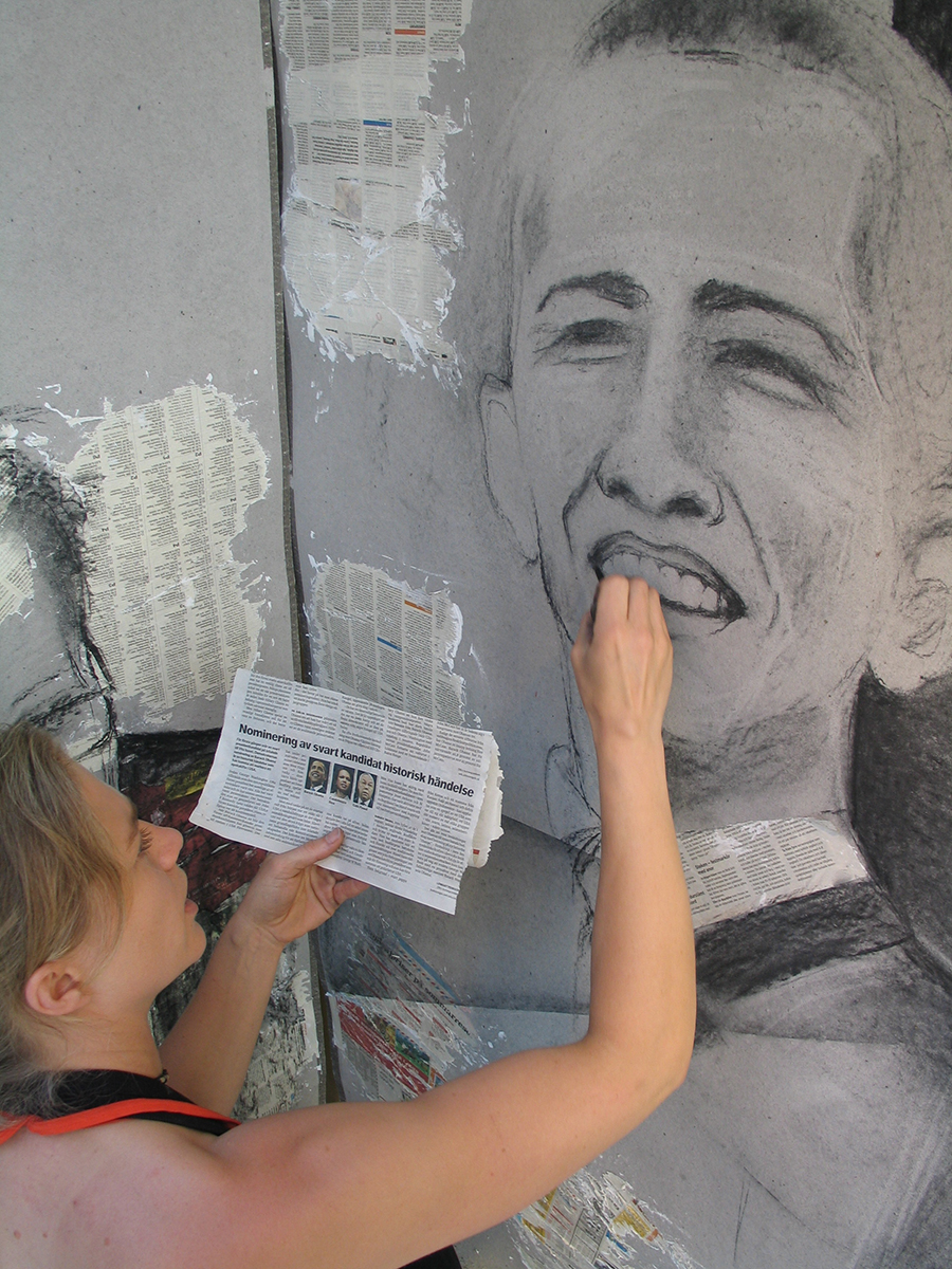 Konstnären har en tidningsartikel i sin hand som har en bild på Barack Obama som hon kollar på för att efterlikna fotot medans hon målar han porträtt på en vägg. 
