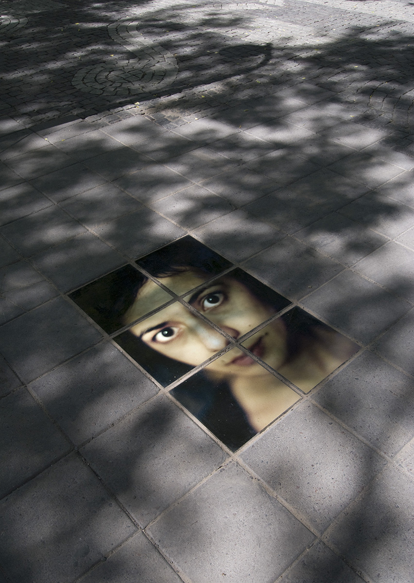 Vägen består av stenplattor men sex stycken av plattorna sticker ut. De har blivit målade på och bildar ett porträtt av en kvinnas ansikte. 