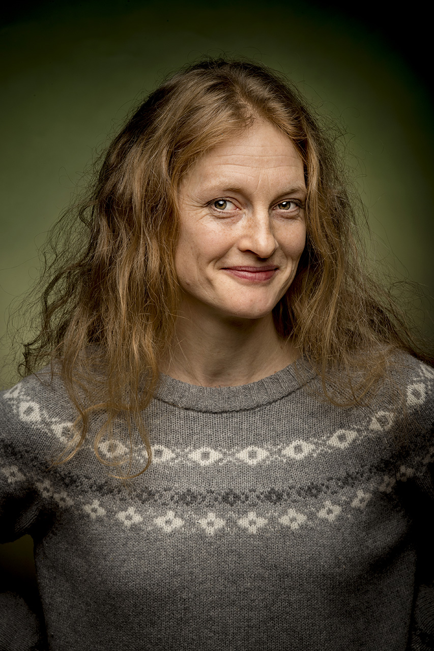 Bilden föreställer en porträttbild av författaren Helena Hedlund. Helena tittar rakt in kameran och är glad och iklädd en mönstrad stickad tröja.