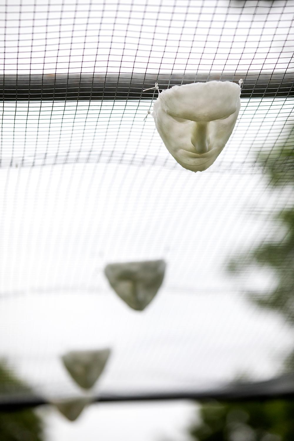 A close-up of one of the white masks hanging from the net and looking down.