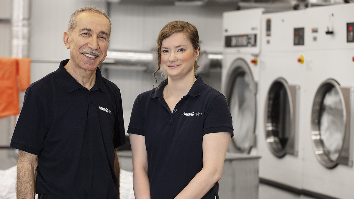 Två leende personer framför tvättmaskiner.