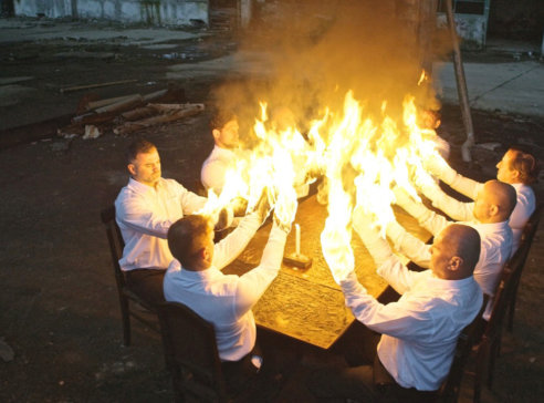 På bilden sitter åtta personer klädda i vit. De sträcker ut sina armar som brinner halvägs ner till armbågarna.