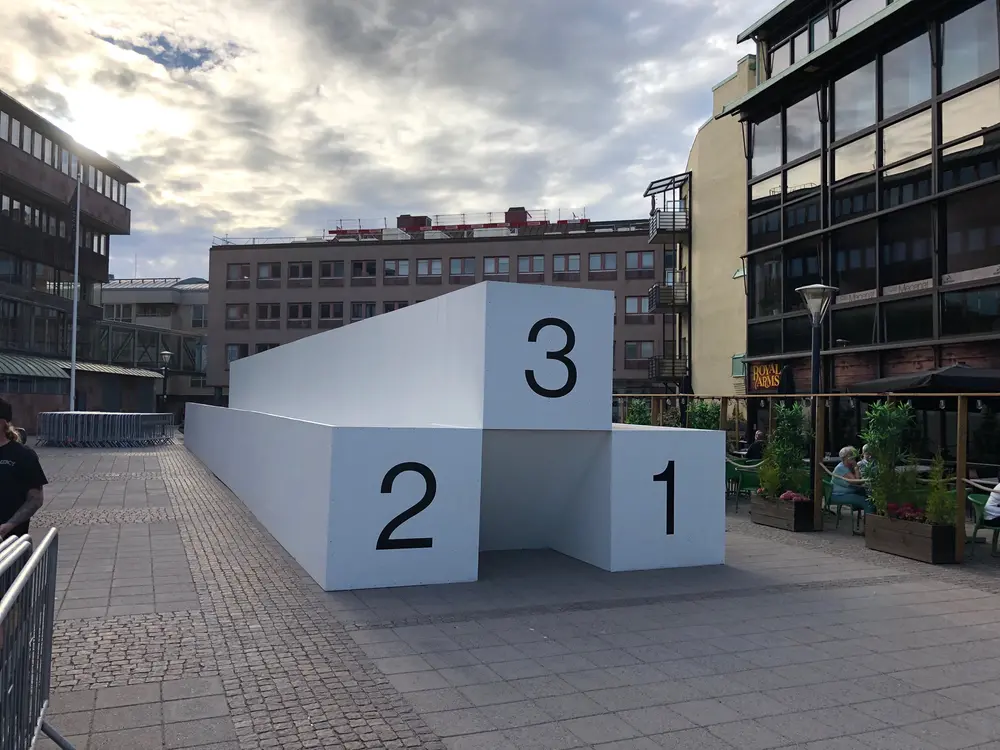 På Olof Palmes Torg står en stor och lång prispall i färgen vit med siffrorna 1, 2 och 3.